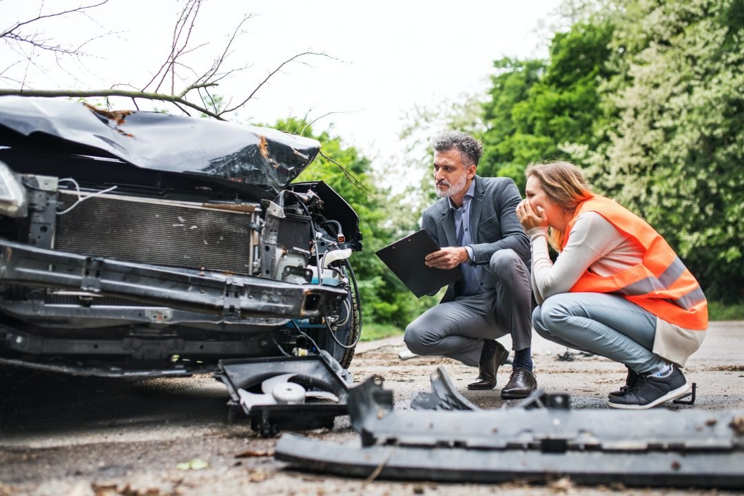 An Insurance Agent and a Woman Driver Looking at the Car on the Road After an Accident